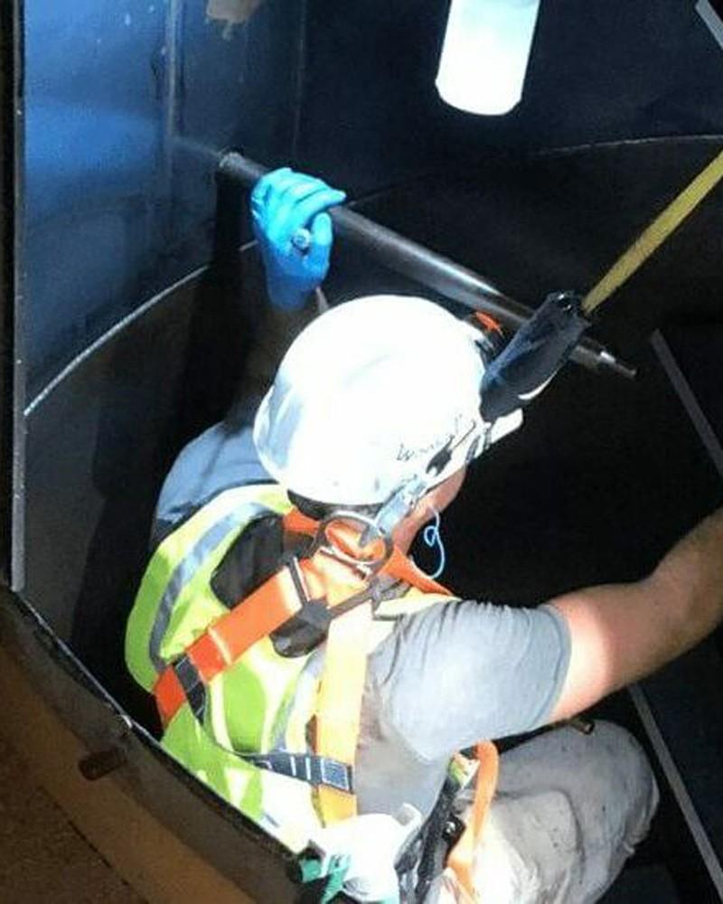 Industrial worker with safety harness and protective gear inside a tank at a facility in Alabama