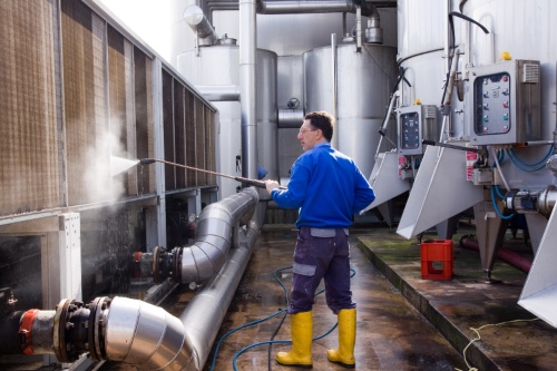 Worker performing hot water pressure washing on industrial surface